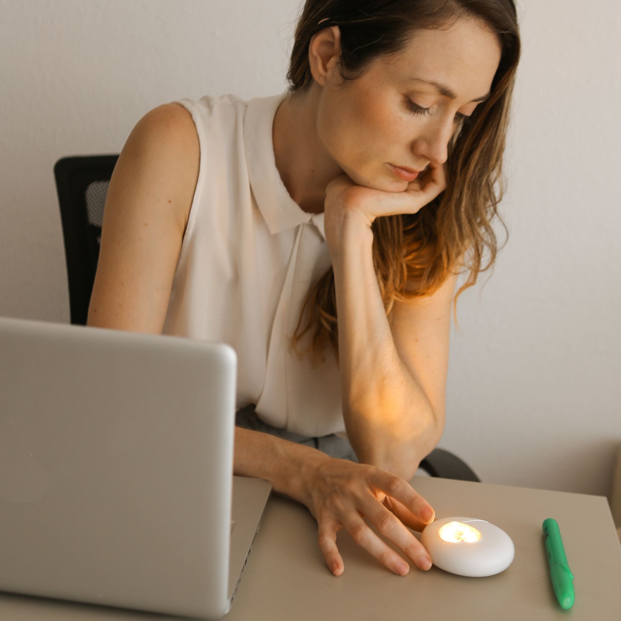 Eine Frau schwenkt ihren Blick vom Notebook hin zum HerzLicht, das auf dem Schreibtisch liegt.